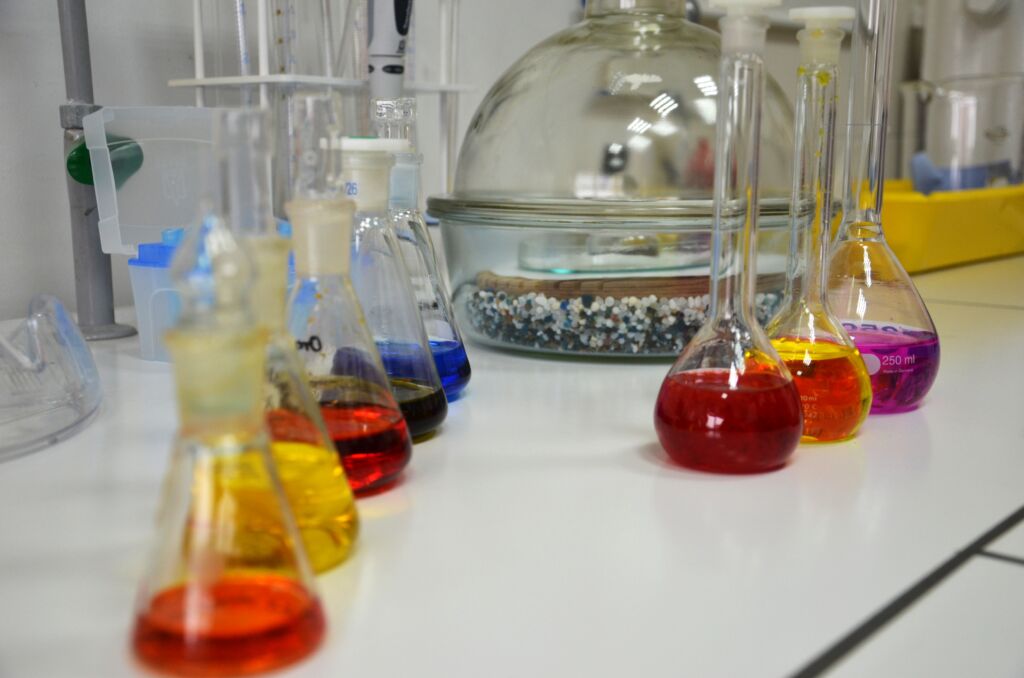 Zdjęcie przedstawiające szkło laboratoryjne z kolorowymi substancjami
