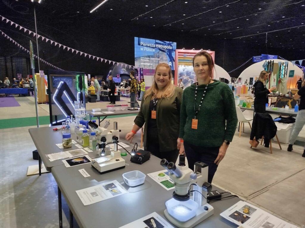 Zdjęcie przedstawia  dwie kobiety pozujące do zdjęcia przed ich stanowiskiem na Śląskim Festiwalu Nauki