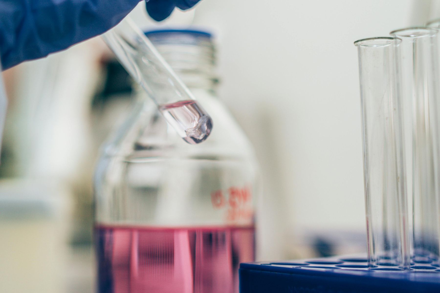 Próbówka z różowa substancją trzymana na tle laboratorium