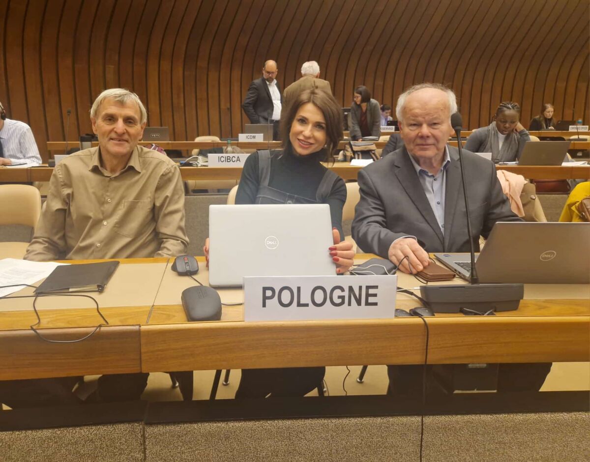 Zdjęcie przedstawia 2 osoby siedzące na auli. Przed nimi kartka z napisem "Pologne"