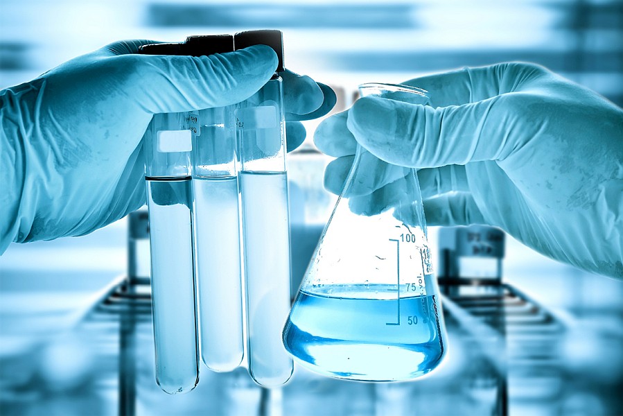 Szkło laboratoryjne w dłoniach naukowca zabezpieczonych rękawicami lateksowymi